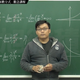 A fully-clothed Changhsumath stands before a chalkboard on which math problems are written.